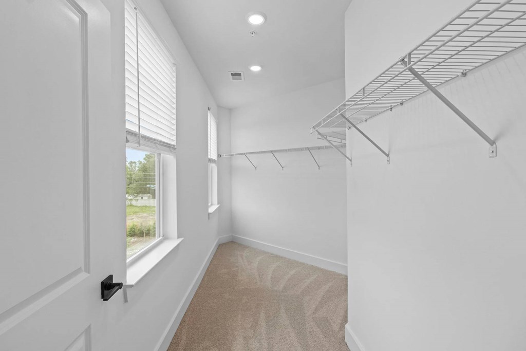A room with a carpeted floor, a window with blinds, and a metal shelving unit.