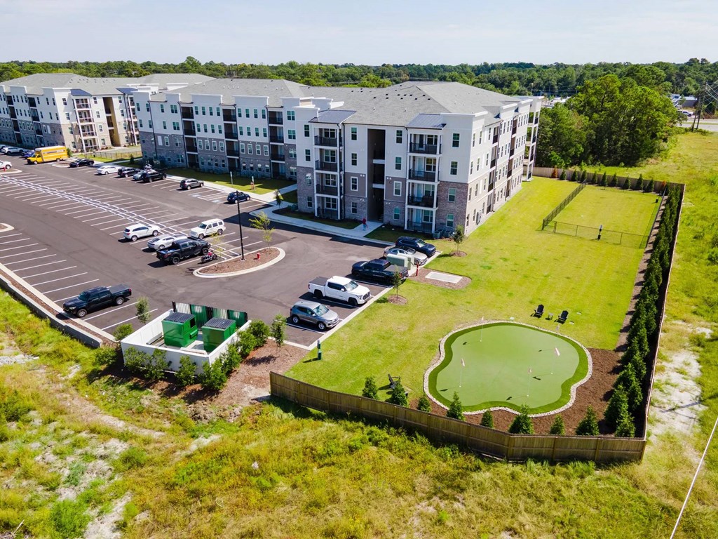 An aerial view of a parking lot in front of a building with a green lawn and a small golf course.