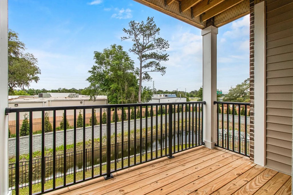 A balcony with a black railing and a wooden floor overlooks a street.