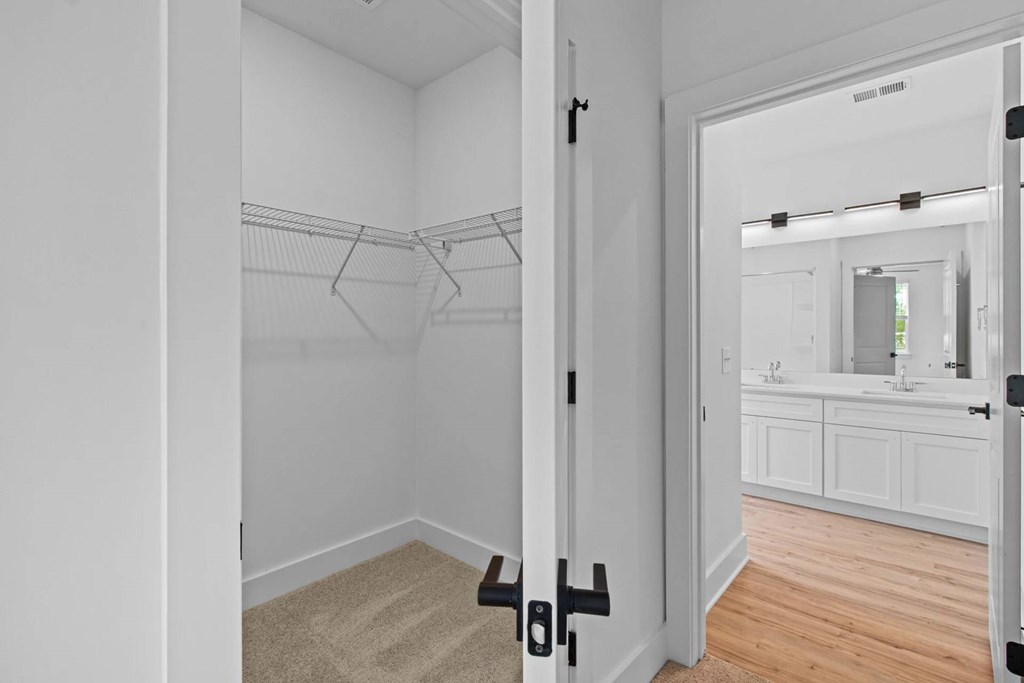 A white closet with a mirror and a bathroom in the background.