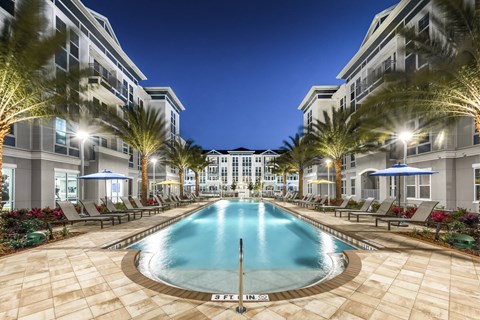 A large swimming pool surrounded by palm trees and lounge chairs at a resort.