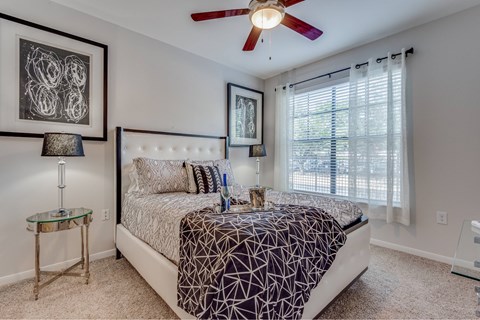 A bedroom with a bed, a ceiling fan, and a table with a lamp.