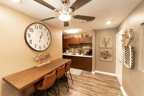 A dining room with a wooden table and chairs, a clock on the wall, and a ceiling fan.