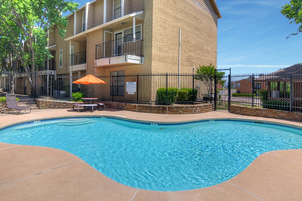 A swimming pool in front of a building with a black fence around it.