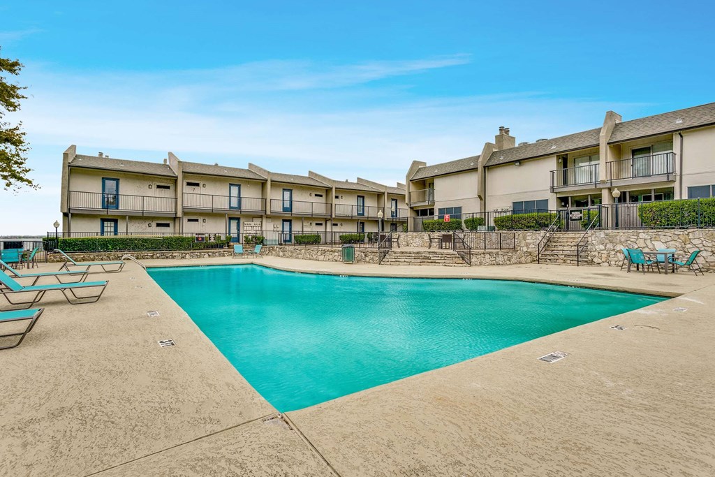 A large swimming pool in front of a building with lounge chairs around it.