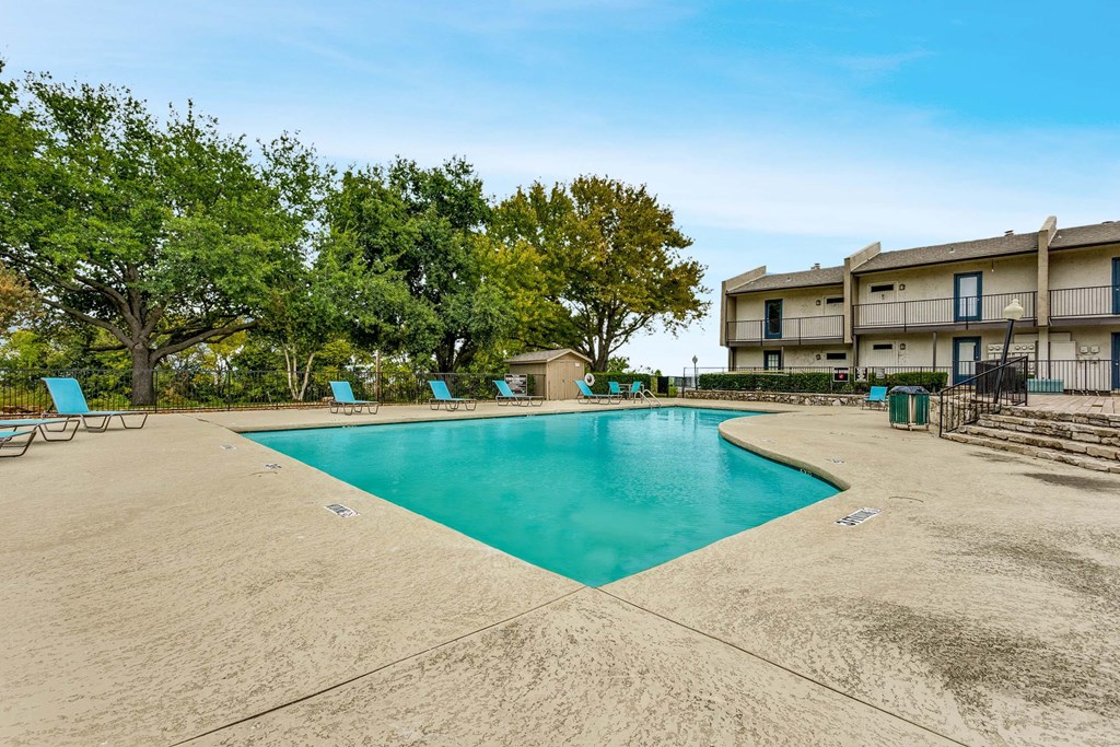 A large swimming pool surrounded by trees and chairs.