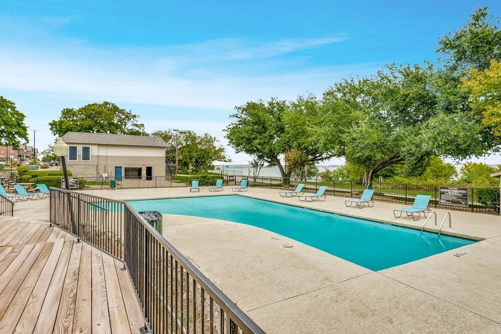 A pool with a deck and a small house in the background.