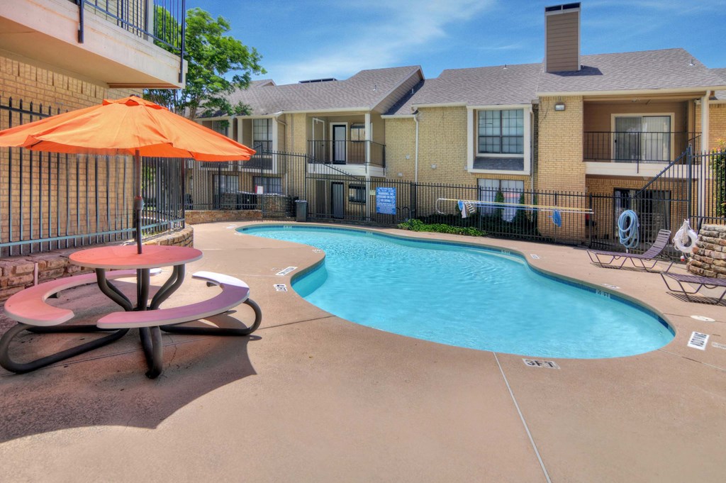 A pool surrounded by a fence and a table with an umbrella.