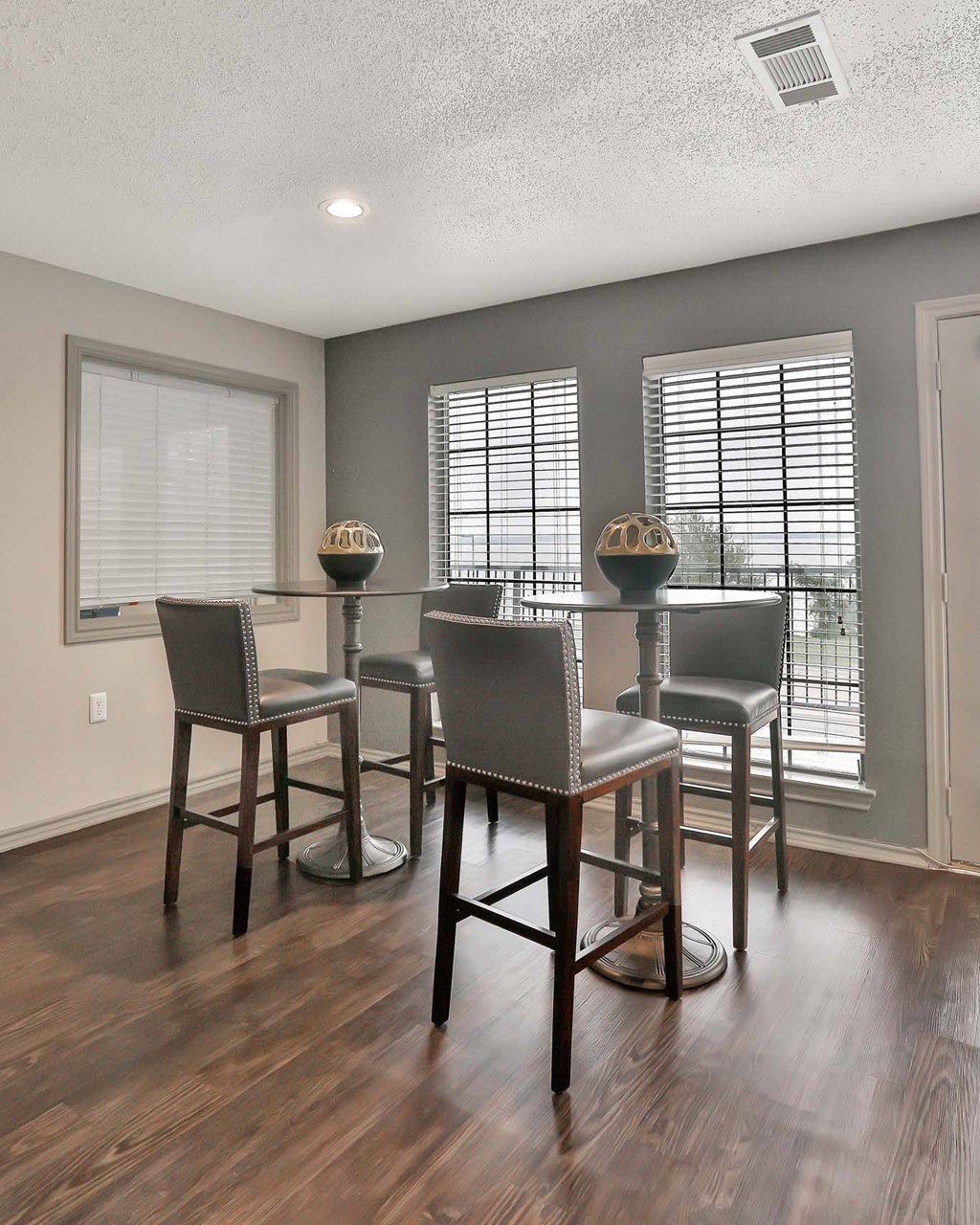 A set of four bar stools with cushioned seats are arranged in a row in front of a window with blinds.