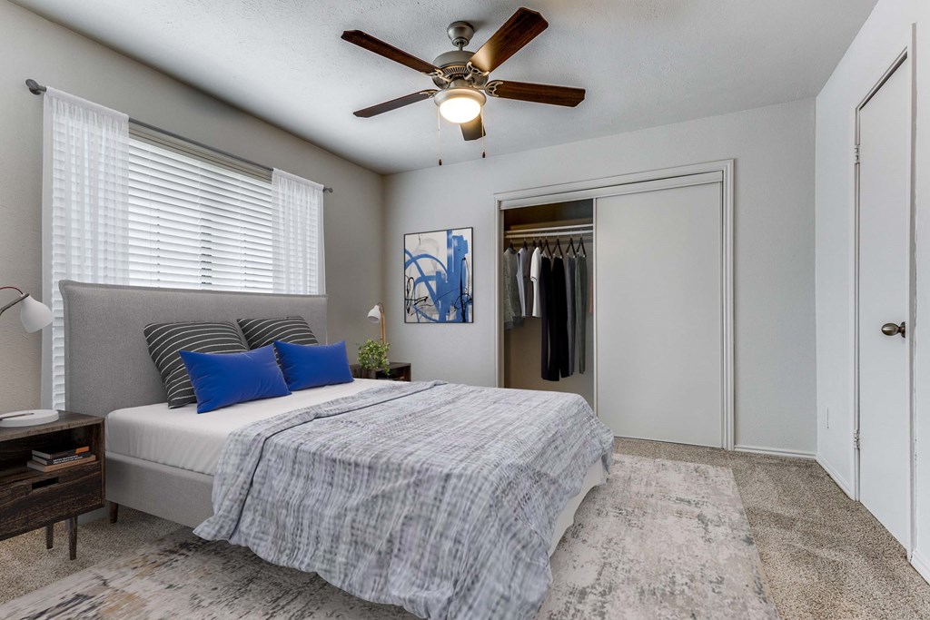 A bedroom with a bed, a ceiling fan, and a painting on the wall.