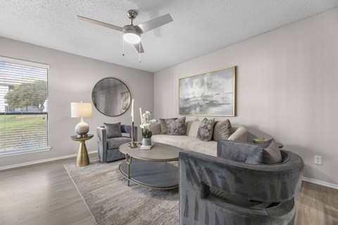 A living room with a grey couch, a round mirror, and a painting on the wall.