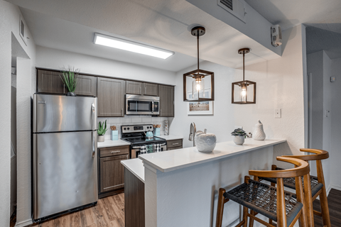A modern kitchen with a stainless steel refrigerator and wooden chairs.