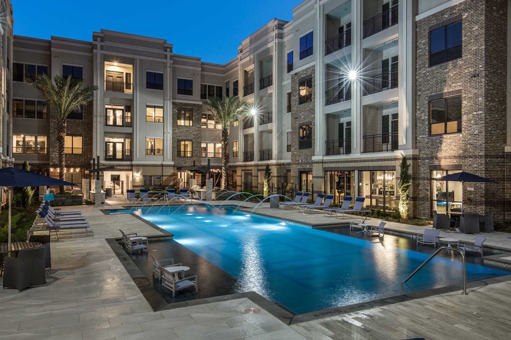 A large swimming pool surrounded by lounge chairs and umbrellas in front of a building.