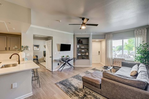 A modern living room with a brown couch and a white kitchen area.