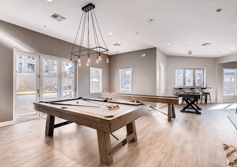 A billiard table is in the middle of a room with a pool table and a foosball table.