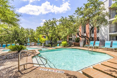 A pool surrounded by trees and chairs.
