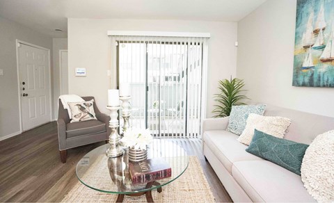 A living room with a grey armchair, a glass coffee table, a white sofa, and a painting on the wall.