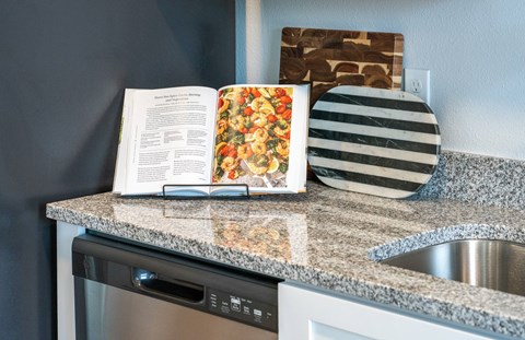 A cookbook sits on a kitchen counter next to a striped plate and a cutting board.