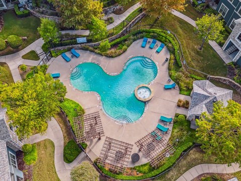 An aerial view of a swimming pool surrounded by a grassy area and trees.