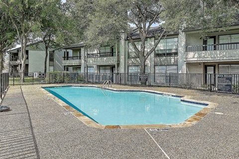 A small pool surrounded by a black fence and trees.