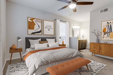A bedroom with a large bed, a ceiling fan, and two artworks on the wall.