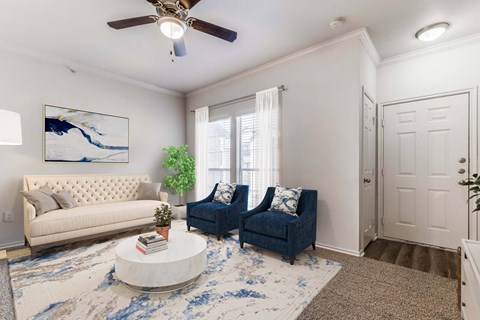 A living room with a white couch, blue chair, and a painting on the wall.