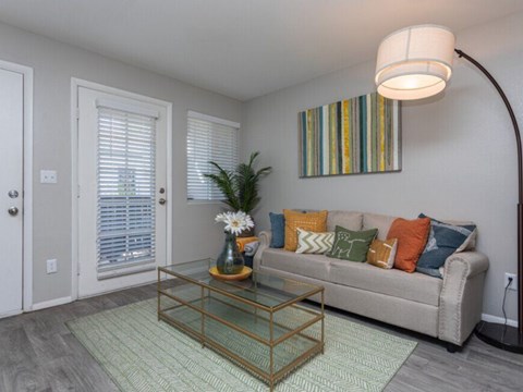A living room with a glass coffee table and a striped picture on the wall.