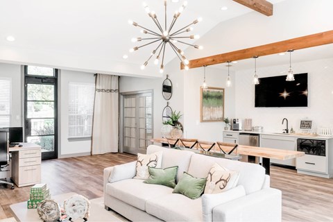 A white couch with green pillows sits in a living room with a wooden floor and a chandelier hanging from the ceiling.