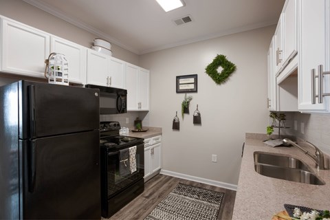 A black refrigerator is in a kitchen with a wreath on the wall.