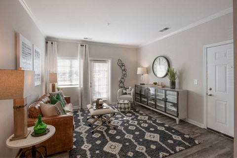 A living room with a brown couch, a white chair, and a rug with a black and white pattern.
