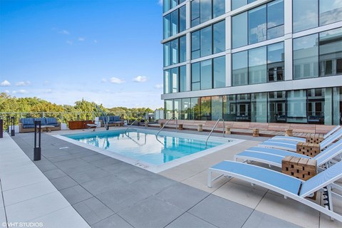 A pool area with sun loungers and a modern building in the background.