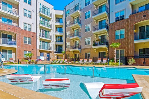 A pool with red and white chairs in front of apartment buildings.