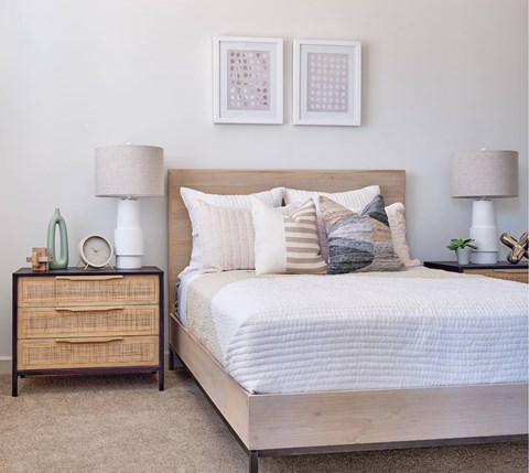 A bedroom with a bed, nightstand, and two framed pictures on the wall.
