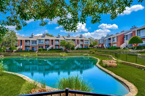 A pond in a residential area surrounded by grass and trees.