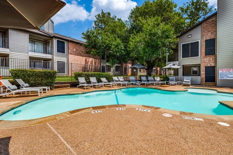 A large swimming pool surrounded by lounge chairs and trees.