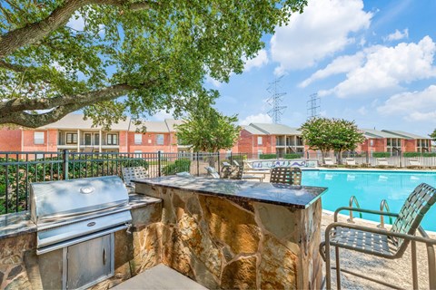 A barbecue grill is on a stone patio next to a swimming pool.