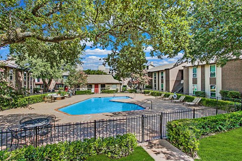 A pool surrounded by a black fence and green bushes.