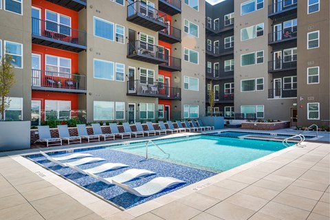 A pool surrounded by lounge chairs in front of our modern apartments in Denver at Canvas on Blake.