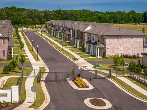 A street view of a residential area with houses on both sides and a gated entrance.