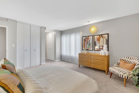 A bedroom with a bed, chair, and a cabinet with a lamp on top.