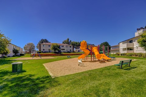 A playground with a yellow slide and green benches at Ridgeview Place rentals in Colorado Springs.