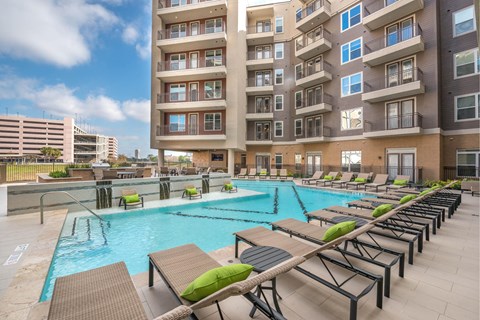 A large swimming pool with lounge chairs and apartment buildings in the background.