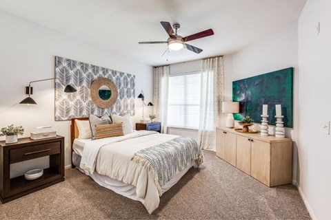 A bedroom with a bed, a ceiling fan, and a painting on the wall.