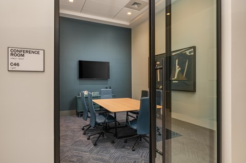 A conference room with a table and chairs and a television on the wall.