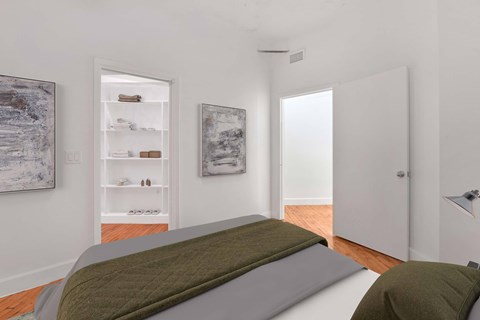 A bedroom with a bed in the foreground and a white wall with a painting on it.