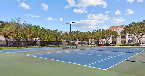 A tennis court surrounded by trees and a building in the background.