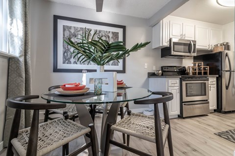 A modern kitchen with a glass dining table set with chairs and a potted plant.