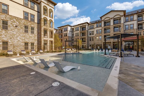 A large outdoor swimming pool surrounded by sun loungers and buildings.