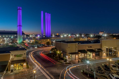 A city street at night with cars driving by and buildings with purple lights.