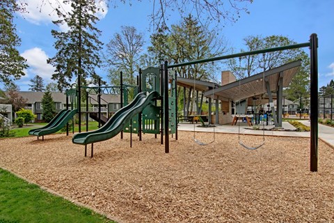 A playground with a green slide and brown sand.